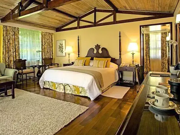 Luxurious bedroom suite at Belmond hotel with four-poster bed, yellow walls, wooden beams, and elegant furnishings overlooking Patagonian landscapes.