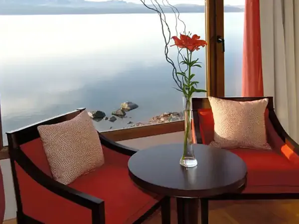 Luxury lakeside suite at Alma del Lago with panoramic water views, red furnishings, and fresh flowers overlooking Patagonian landscape.
