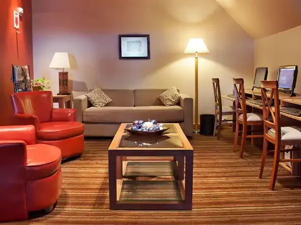 Modern hotel lounge at Mirador del Lago with red armchairs, beige sofa, wooden tables, and work stations overlooking Patagonian landscape.