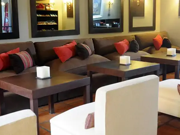 Modern lounge area with brown leather seating, red accent pillows, and contemporary furnishings at Legado Mítico hotel.