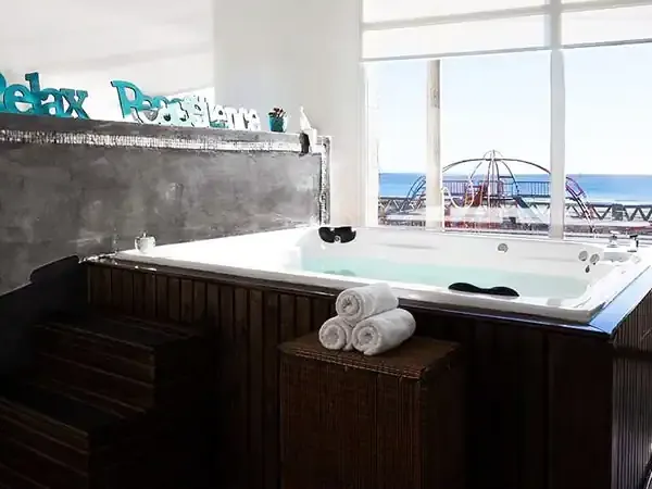 Luxury spa bathroom with turquoise jetted tub overlooking amusement park and ocean coastline at Puerto Madryn resort.
