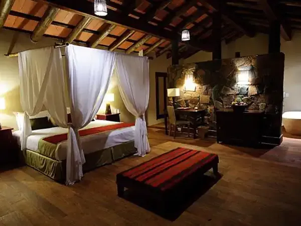 Luxurious canopy bed in a spacious bedroom at Loi Suites hotel with warm lighting and rustic wooden beams.