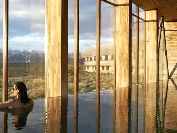 Woman relaxing in an infinity pool overlooking the Patagonian landscape with mountains and estancia buildings in Tierra del Fuego.