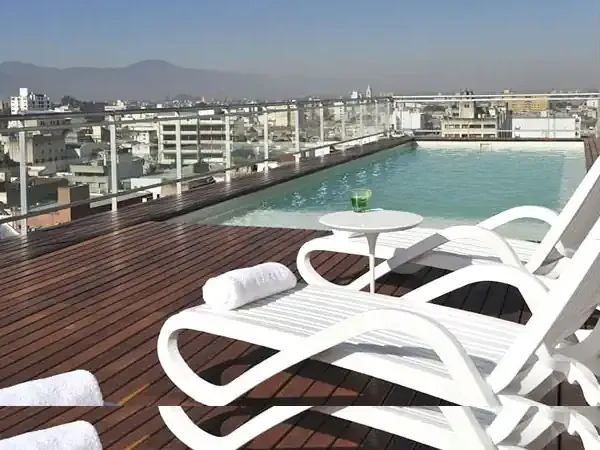 Rooftop pool with lounge chairs overlooking a South American city skyline and mountains.