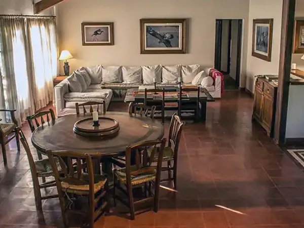 Spacious rustic lodge interior at Rincón del Socorro with wooden dining table, sectional sofa, and natural light from large windows.