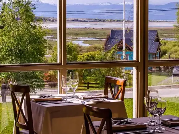 Elegant dining room with panoramic windows overlooking Patagonian lakes, mountains, and valleys at Mirador del Lago.