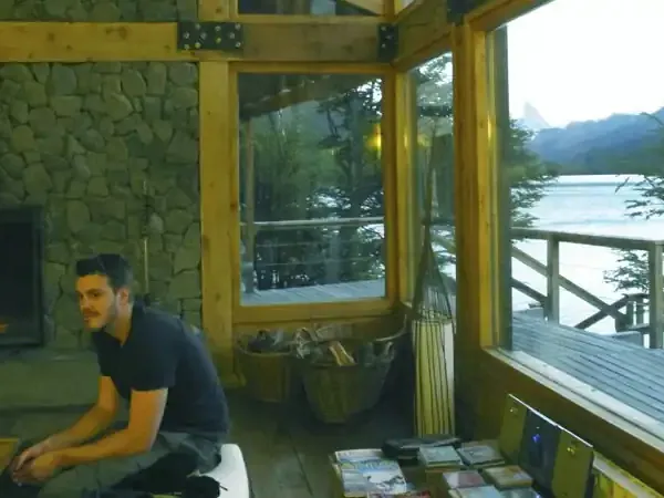 Man relaxing by fireplace in modern lodge with lake and mountain views at Aguas Arriba.