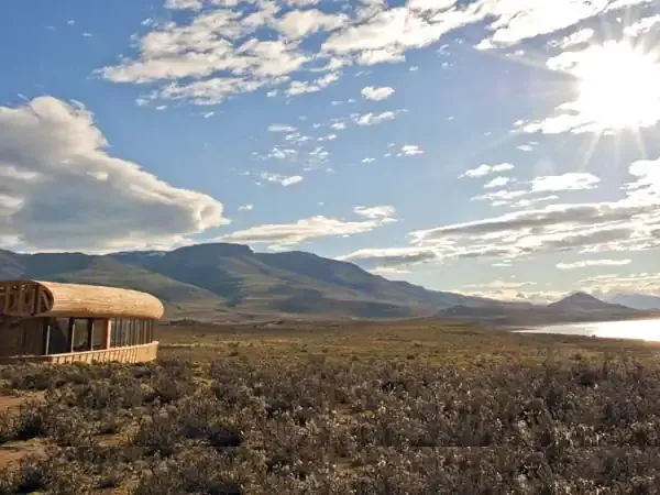 Tierra Patagonia's distinctive architecture blends into the vast steppe landscape with mountains and lake under dramatic Patagonian skies.