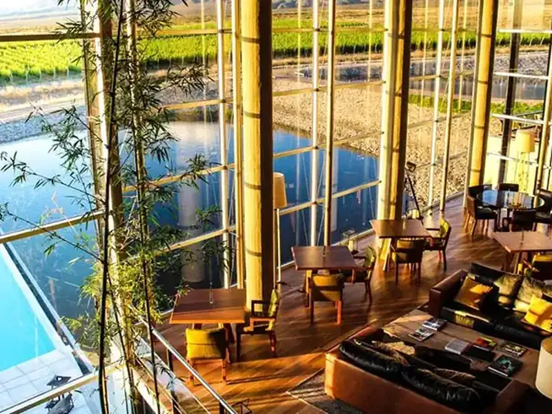 Modern lodge with floor-to-ceiling windows overlooking vineyard pools and agricultural fields in Casa de Uco, Mendoza wine region.