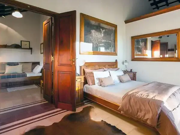 Luxurious bedroom suite at Rincón del Socorro with wooden furnishings, white linens, and mirrored doors overlooking adjacent rooms.