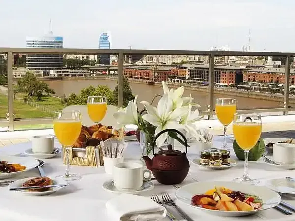 Elegant outdoor brunch overlooking the Río de la Plata in Puerto Madero, Buenos Aires, with fresh fruit, pastries, and orange juice.