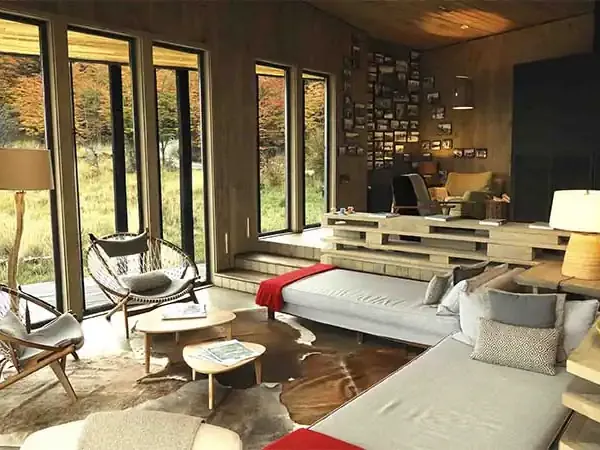 Modern Patagonian lodge bedroom with floor-to-ceiling windows overlooking natural landscape, featuring minimalist design and comfortable furnishings.