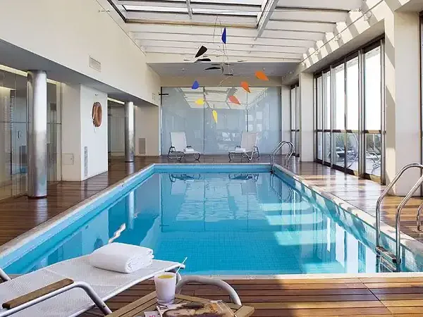 Luxurious indoor swimming pool at a Madero hotel with floor-to-ceiling windows overlooking modern architecture and city views.