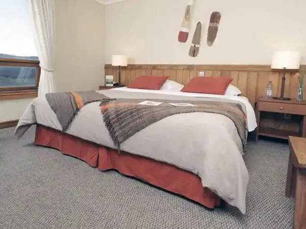 Rustic hotel bedroom with wooden headboard, red accents, and window view at Hotel Las Torres in Patagonia.