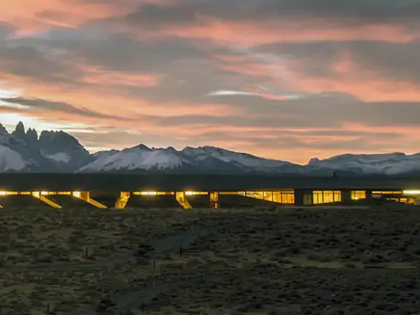 Explora Hotel Tierra Patagonia glows at dusk beneath snow-capped Patagonian peaks and dramatic sunset sky.