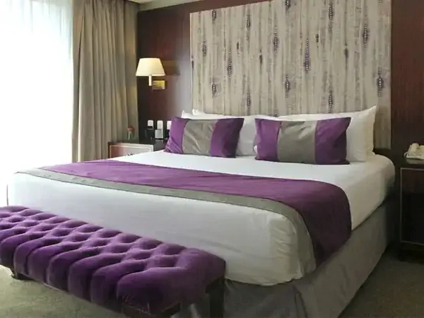 Luxury hotel bedroom at Iguazú Grand with purple and grey accents, modern furnishings, and elegant lighting.