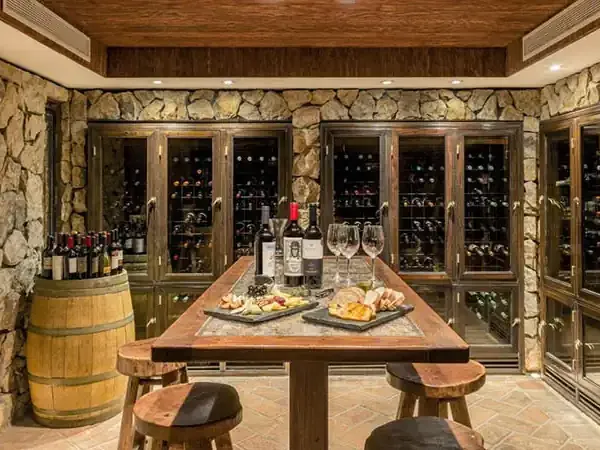 Luxurious wine cellar at Sheraton Mendoza featuring temperature-controlled glass cabinets, wooden tasting table, and stone walls.
