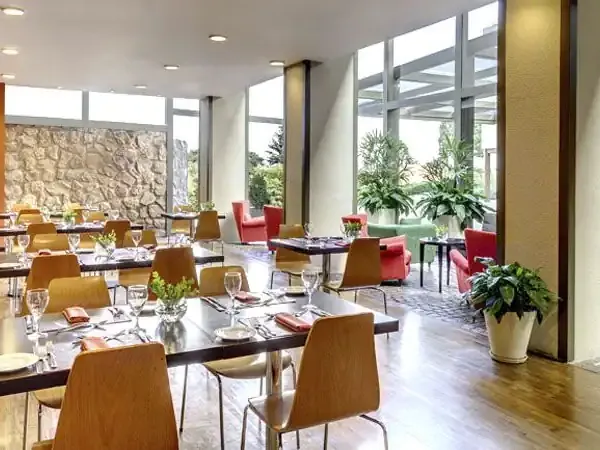 Modern restaurant dining room at Sheraton hotel with contemporary wood furnishings, stone accents, and expansive windows overlooking gardens.