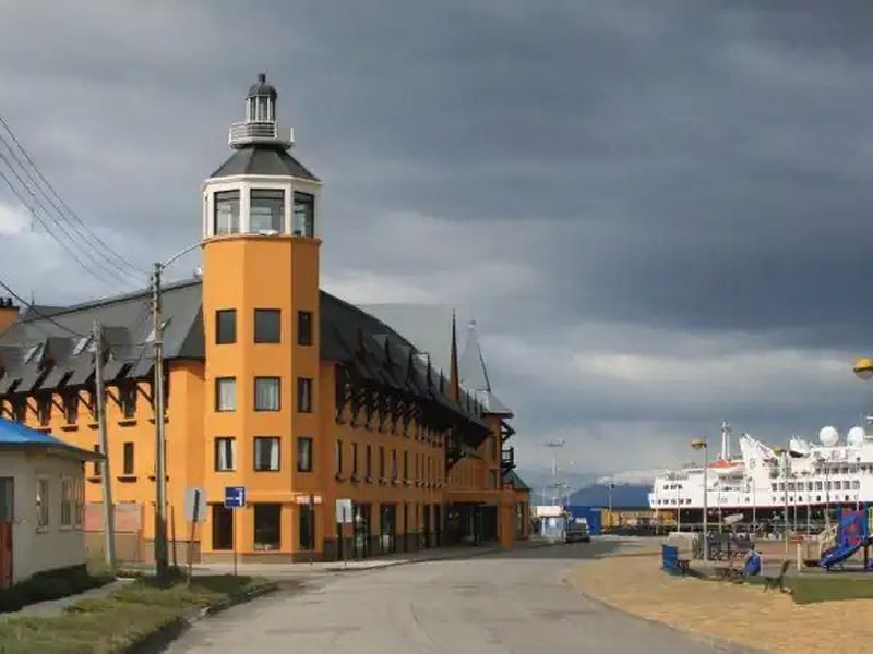 Distinctive orange building with tower overlooks Puerto Natales waterfront under dramatic cloudy Patagonian sky.