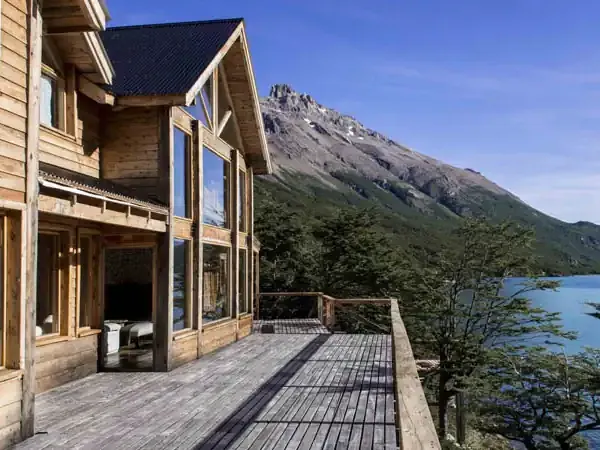 Luxury lodge deck overlooks turquoise lake with snow-capped mountain peak in Patagonia.