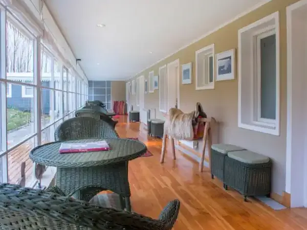 Sunlit interior hallway with wicker furniture, framed artwork, and views of Patagonian landscape through large windows.