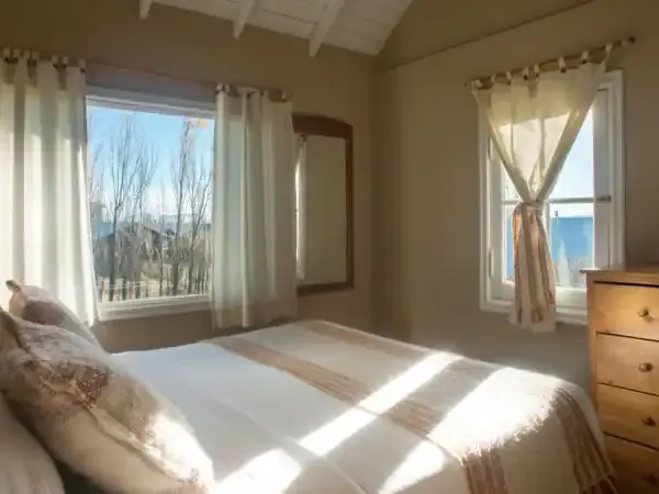 Bright, airy bedroom at Los Ponchos with large windows overlooking Patagonian landscape, wooden dresser, and natural light.