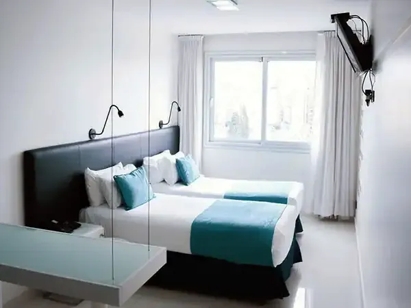 Modern hotel bedroom with teal accents, mirrored walls, and large windows at Cyan Recoleta in Buenos Aires.