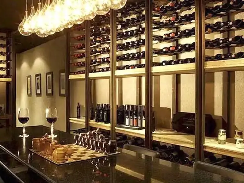 Elegant wine cellar with illuminated bottle displays, chess set, and wine glasses at a polished counter.