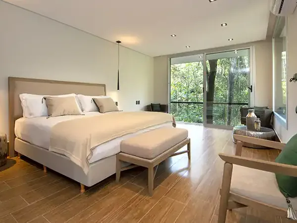 Luxurious modern bedroom at Selvaje Lodge with king bed, forest views through floor-to-ceiling windows, and contemporary furnishings.