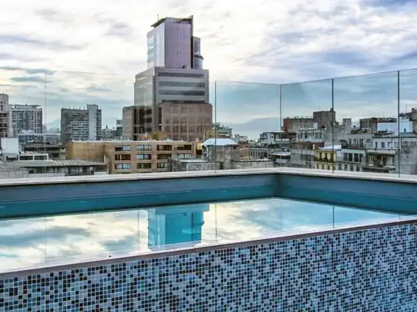 Rooftop pool overlooking Santiago's downtown skyline with modern and historic architecture under cloudy skies.