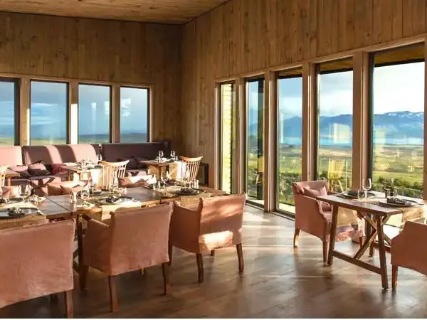 Luxury lodge interior with panoramic windows overlooking vast Patagonian valley and mountain landscape in natural daylight.
