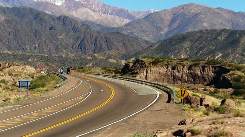 Scenic mountain road with yellow center lines curving through Andean valleys near Villavicencio, Mendoza.