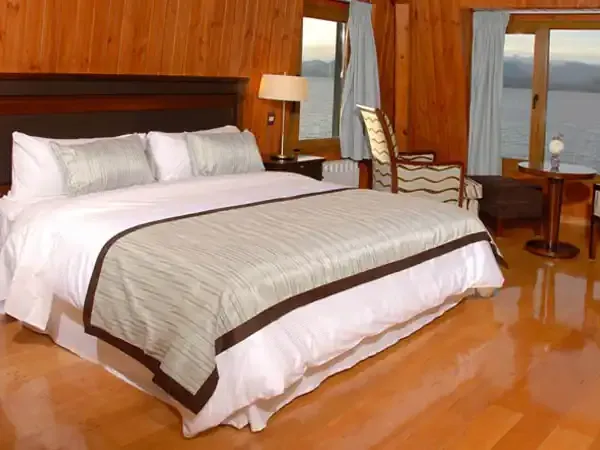 Luxury lakeside bedroom with wooden paneling, large bed, and panoramic water views at Alma del Lago resort.
