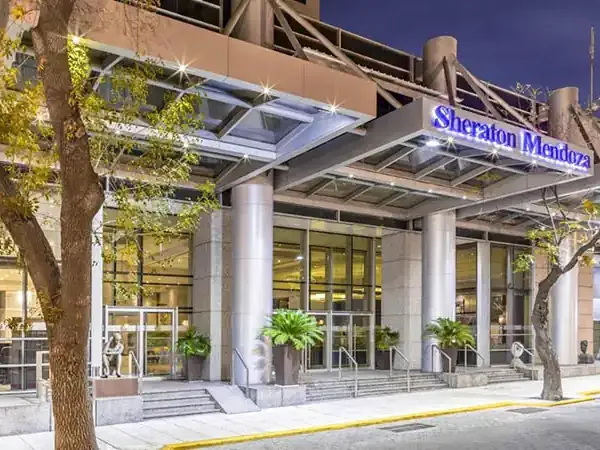Sheraton Mendoza hotel entrance with modern architecture, illuminated signage, and landscaped courtyard at dusk.