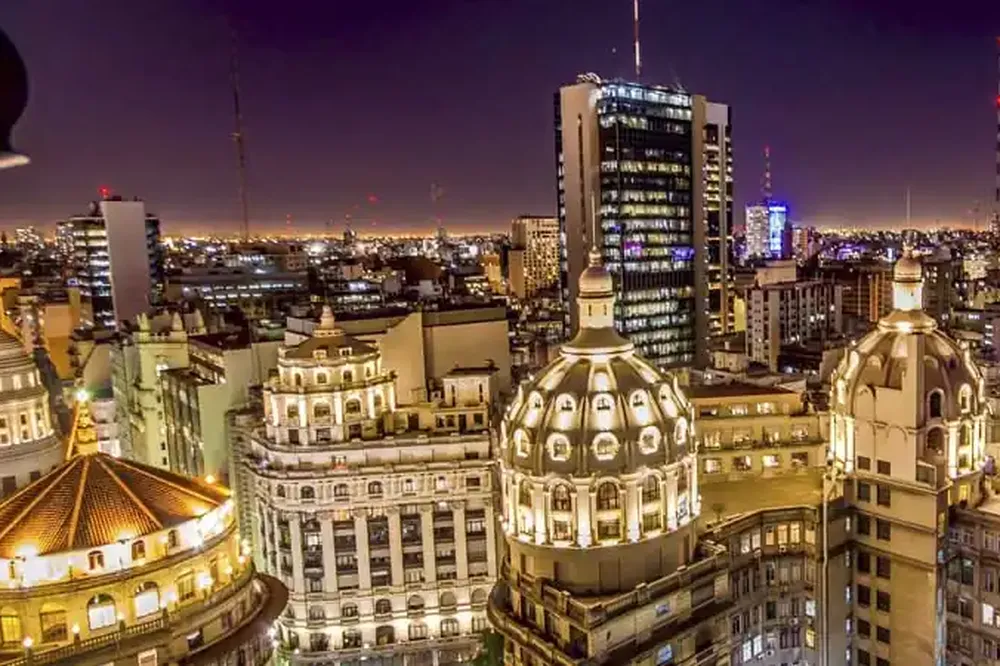 Buenos Aires illuminated at dusk with ornate dome architecture and modern skyline buildings.
