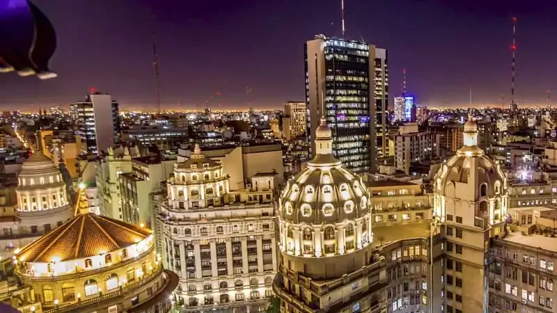 Buenos Aires illuminated at dusk with ornate dome architecture and modern skyline buildings.
