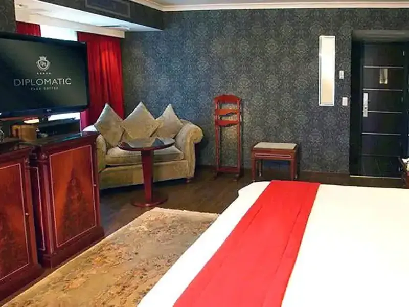 Luxury hotel suite at Diplomatic with elegant red-accented furnishings, flat-screen TV, and sophisticated décor.