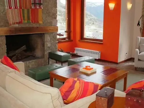 Bright orange and cream living room at Los Cerros Boutique Hotel with fireplace, panoramic mountain views, and colorful Patagonian textiles.
