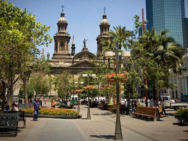 Historic Plaza de Armas in Santiago de Chile with cathedral, palm trees, and modern skyline on a sunny day.