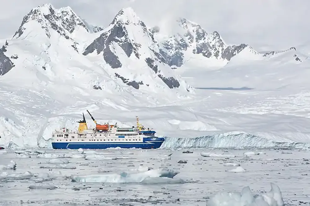 Expedition cruise ship navigates icy waters near snow-capped peaks in the Antarctic Circle.