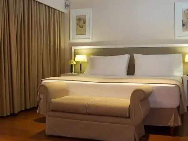 Elegant hotel bedroom with queen bed, cream bedding, warm lighting, wooden floors, and floor-to-ceiling curtains in a luxury accommodation.