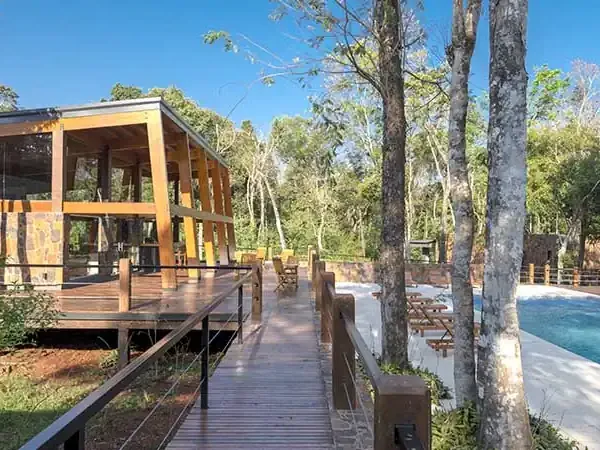 Modern wooden lodge nestled in lush forest with swimming pool and deck walkway at Selvaje Lodge, Patagonia.