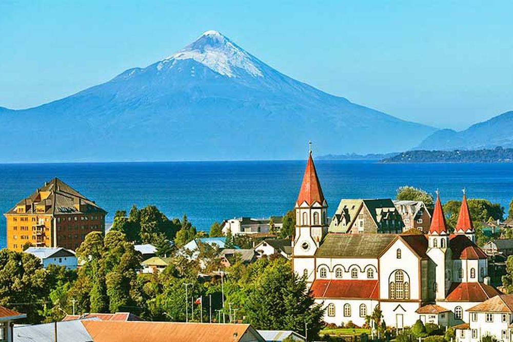 Puerto Varas lakeside town with snow-capped Osorno volcano, German-style churches, and colorful architecture overlooking blue waters.