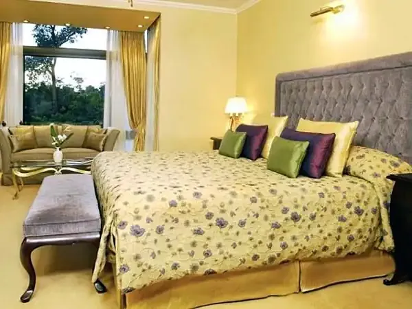 Luxurious bedroom suite at Iguazú Grand hotel with yellow walls, bay window seating area, and forest views.