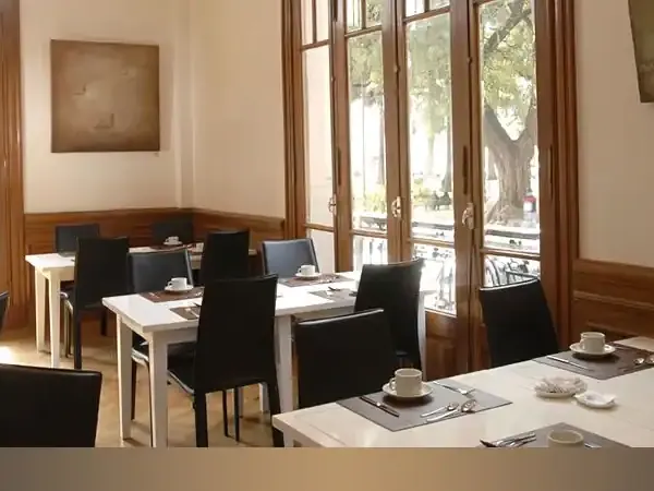 Modern hotel dining room with black chairs, white tables, and large windows overlooking a tree-lined street in Patagonia.
