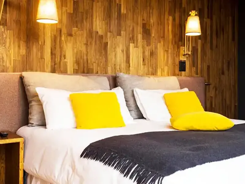 Modern hotel bedroom with wooden walls, comfortable bed, yellow accent pillows, and warm lighting at Casa de Ucó.