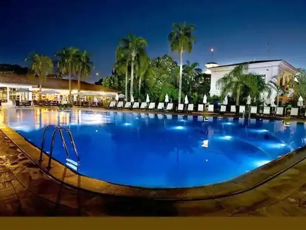 Illuminated resort pool at twilight surrounded by palm trees, loungers, and colonial architecture in Patagonia.