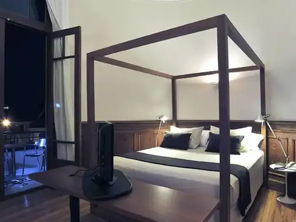 Elegant four-poster bed in a modern luxury hotel bedroom with dark wood furnishings and contemporary design elements.