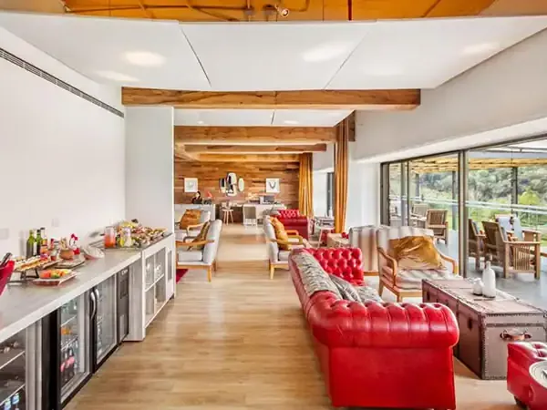 Modern luxury lodge interior with red furnishings, wooden beams, and panoramic windows overlooking Iguazú Falls landscape.