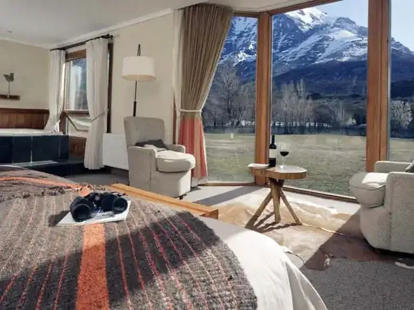 Luxurious hotel suite at Las Torres with panoramic snow-capped mountain views, modern furnishings, and floor-to-ceiling windows overlooking Patagonian landscape.